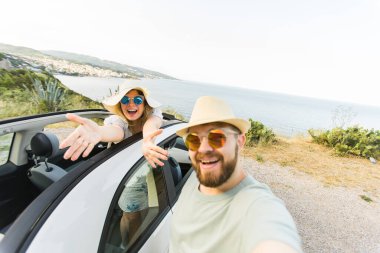 Mutlu ve güzel bir çift tatilde üstü açık bir arabayla selfie çektiriyorlar. Kiralık arabalar ve tatil konsepti