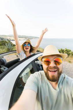 Mutlu ve güzel bir çift tatilde üstü açık bir arabayla selfie çektiriyorlar. Kiralık arabalar ve tatil konsepti