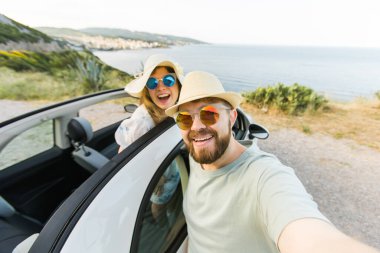 Mutlu ve güzel bir çift tatilde üstü açık bir arabayla selfie çektiriyorlar. Kiralık arabalar ve tatil konsepti