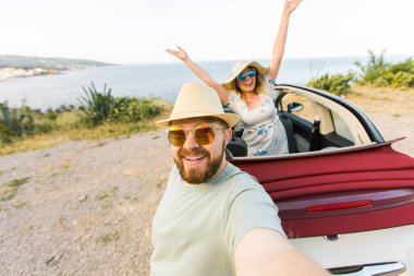 Mutlu ve güzel bir çift tatilde üstü açık bir arabayla selfie çektiriyorlar. Kiralık arabalar ve tatil konsepti