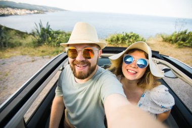 Romantik çift, okyanus ya da deniz kıyısındaki kiralık Cabrio arabasında akıllı telefon kamerasıyla selfie çekiyor, yaz tatilinin tadını çıkarıyor ve hafta sonları deniz kenarında cep telefonuyla dinlenirken fotoğraf çekiyor.