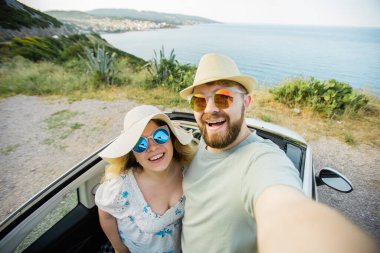 Romantik çift, okyanus ya da deniz kıyısındaki kiralık Cabrio arabasında akıllı telefon kamerasıyla selfie çekiyor, yaz tatilinin tadını çıkarıyor ve hafta sonları deniz kenarında cep telefonuyla dinlenirken fotoğraf çekiyor.