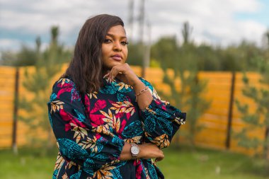 Arka bahçede dikilen kırmızı günlük giysili güzel Afrikalı Amerikalı kadının yaz portresi. Kenar mahalle yaşam tarzı ve hafta sonları kırsal konseptte rahatlama