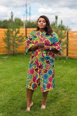 Arka bahçede dikilen kırmızı günlük giysili güzel Afrikalı Amerikalı kadının yaz portresi. Kenar mahalle yaşam tarzı ve hafta sonları kırsal konseptte rahatlama