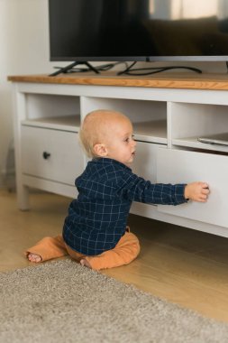 Toddler baby boy open cabinet drawer with his hand. Child explore what is in cabinet. Baby curiosity and child development stages concept