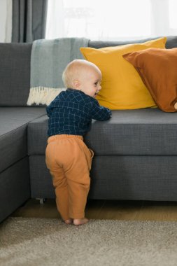 Caucasian baby newborn infant making first steps. Cute toddler kid child son boy learning walking creeping on living room. Childcare and childhood