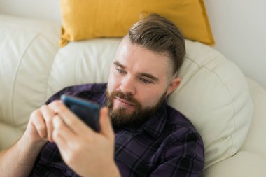Sıkkın tembel adam rahatladı ve evde yalnız zaman geçirmek için akıllı telefon kullandı. Sosyal medya ve alet bağımlılığı.