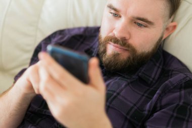 Sıkkın tembel adam rahatladı ve evde yalnız zaman geçirmek için akıllı telefon kullandı. Sosyal medya ve alet bağımlılığı.