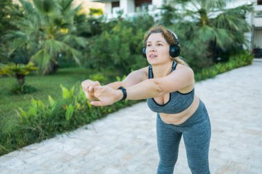 Eşofmanlı sevimli şişman kadın dışarıda spor salonunun dış görünüş portresiyle meşgul. Genç şişman kadın sıcak bir yaz gününde dışarı atlıyor. Sağlıklı yaşam tarzı ve kilo kaybı.