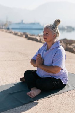 Deniz ve sahil kenarında meditasyon yapan dikkatli son sınıf öğrencisi bir kadın. Sağlık ve yoga konsepti.