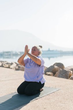 Deniz ve sahil kenarında meditasyon yapan dikkatli son sınıf öğrencisi bir kadın. Sağlık ve yoga konsepti.