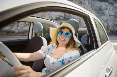 Cabrio 'daki yaz yolculuğunun tadını çıkaran, şapkalı ve güneş gözlüklü, gülümseyen sarışın kadın. Özgürlük için. Seyahat et. Turizm. Tatil.