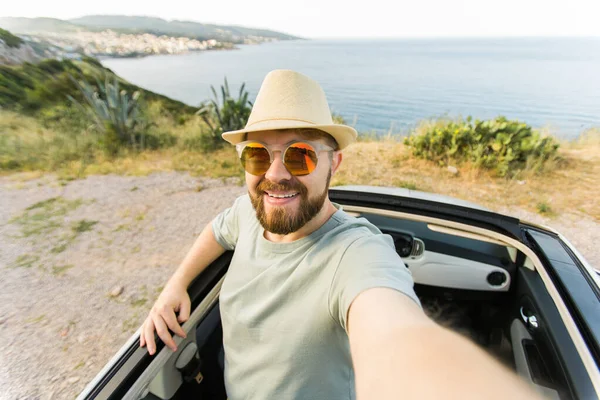 Yolculuk, eğlence ve teknoloji konsepti. Cabriolet 'te araba süren ve akıllı telefonla selfie çeken mutlu adam.