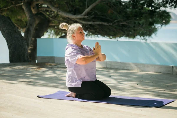 Stock image Senior woman in stretching position by the sea at morning. Elderly woman doing yoga on beach.