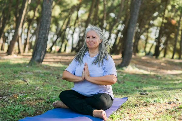 stock image Senior woman in stretching position by the sea at morning. Elderly woman doing yoga on beach.