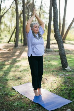 Sabahları deniz kenarında kıdemli bir kadın esneme pozisyonu alıyor. Yaşlı kadın plajda yoga yapıyor..