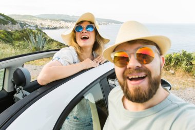 Romantik çift, okyanus ya da deniz kıyısındaki kiralık Cabrio arabasında akıllı telefon kamerasıyla selfie çekiyor, yaz tatilinin tadını çıkarıyor ve hafta sonları deniz kenarında cep telefonuyla dinlenirken fotoğraf çekiyor.