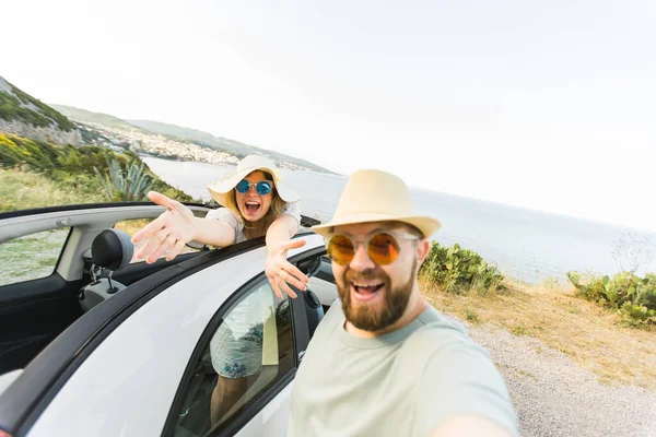 stock image Happy beautiful couple in love taking a selfie portrait driving a convertible car on the road at vacation. Rental cars and vacation concept