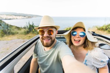 Mutlu ve güzel bir çift tatilde üstü açık bir arabayla selfie çektiriyorlar. Kiralık arabalar ve tatil konsepti