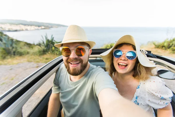 Mutlu ve güzel bir çift tatilde üstü açık bir arabayla selfie çektiriyorlar. Kiralık arabalar ve tatil konsepti
