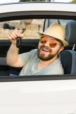 Araba şoförü gülümsüyor. Yeni araba anahtarlarını ve arabasını gösteriyor. Sakallı adam yaz tatilinde kiralık Cabrio kullanıyor.