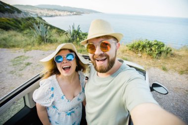 Romantik çift, okyanus ya da deniz kıyısındaki kiralık Cabrio arabasında akıllı telefon kamerasıyla selfie çekiyor, yaz tatilinin tadını çıkarıyor ve hafta sonları deniz kenarında cep telefonuyla dinlenirken fotoğraf çekiyor.