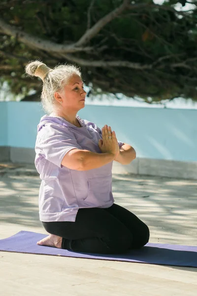 stock image Mature elderly woman with dreadlocks doing pose during yoga training in park on summer day. Healthy active senior female practicing asana on mat in morning on fresh air