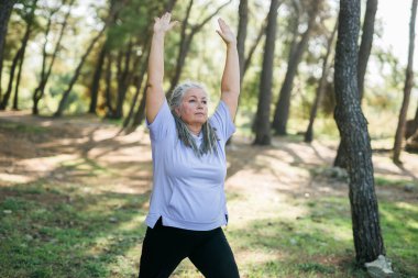 Olgun, gri saçlı, rastalı kadın parkta eğitim görüyor, yoga ya da spor yapıyor - refah ve sağlıklı yaşam tarzı.