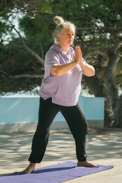 stock image Serious aged woman in with dreadlocks hairstyle standing on a beach against sea with raised arms while practicing pose during sunny day