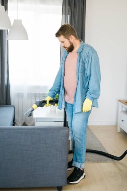 Man holding modern washing vacuum cleaner and cleaning dirty sofa with professionally detergent. Professional springclean at home