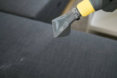 Man in protective rubber glove cleaning sofa with professionally extraction method with washing vacuum cleaner. Early spring regular cleanup. Commercial cleaning company