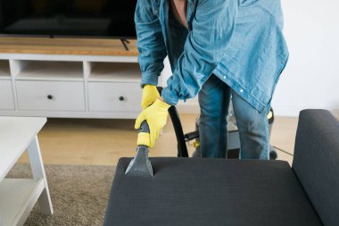Man holding modern washing vacuum cleaner and cleaning dirty sofa with professionally detergent. Professional springclean at home