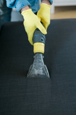 Man in protective rubber glove cleaning sofa with professionally extraction method with washing vacuum cleaner. Early spring regular cleanup. Commercial cleaning company
