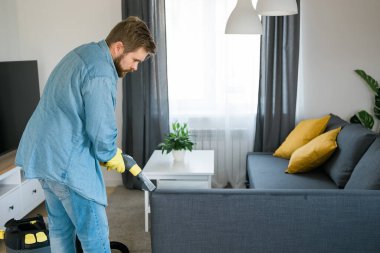 Man holding modern washing vacuum cleaner and cleaning dirty sofa with professionally detergent. Professional springclean at home