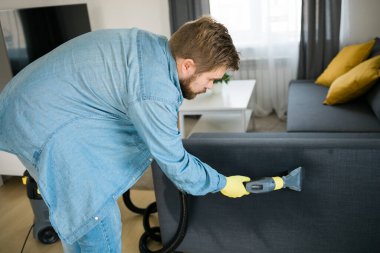 Man in protective rubber glove cleaning sofa with professionally extraction method with washing vacuum cleaner. Early spring regular cleanup. Commercial cleaning company