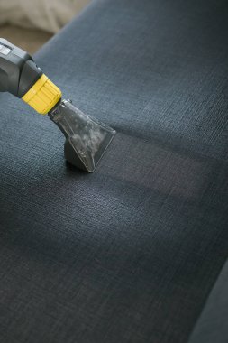Man holding modern washing vacuum cleaner and cleaning dirty sofa with professionally detergent. Professional springclean at home