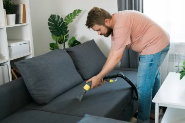 Man holding modern washing vacuum cleaner and cleaning dirty sofa with professionally detergent. Professional springclean at home