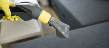 Temizlik şirketi çalışanı, profesyonel malzemelerle mobilyaların tozunu alıyor. Erkek kol temizleme koltuğu ve elektrikli süpürge.