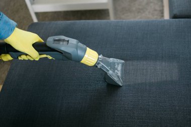 Temizlik şirketi çalışanı, profesyonel malzemelerle mobilyaların tozunu alıyor. Erkek kol temizleme koltuğu ve elektrikli süpürge.