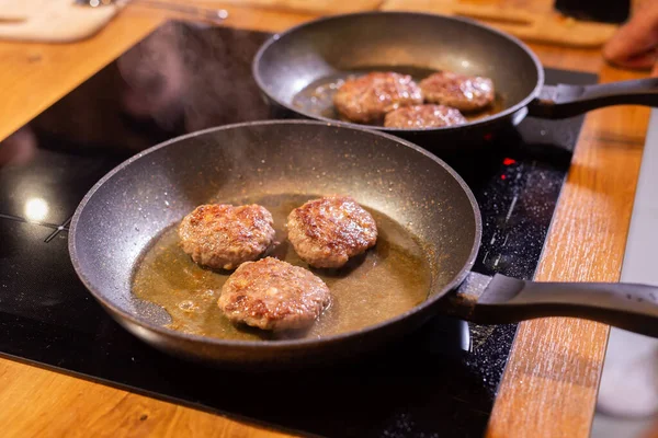 Meat burgers or cutlet-shaped patty being shallow fried in oil on a frying pan close up