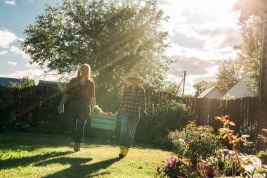 Beautiful women farmer holding ripe organic vegetables in wooden box in garden. Happy female gardener harvesting agricultural product for online selling