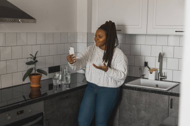 Happy modern African American young girl talking on video chat and sit home communication concept. Smiling hipster girl making self portrait on her telephone at home