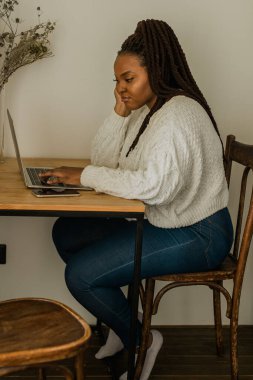 Cheerful african american woman using laptop while sitting on chair in living room - student, video call and working at home