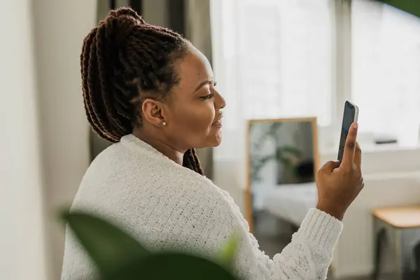 stock image Portrait of good-looking African female student dressed casually holding mobile phone and typing messages and communicating with friends social networks using high-Internet connection.