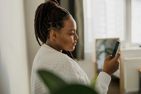 stock image Portrait of good-looking African female student dressed casually holding mobile phone and typing messages and communicating with friends social networks using high-Internet connection.