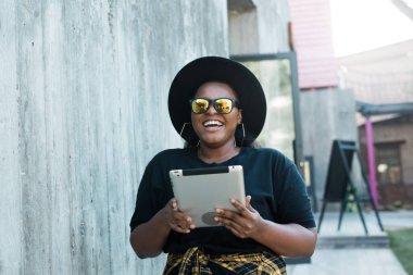 Güzel kıvırcık Afrikalı Amerikalı bir kızın portresi. Arka planda duruyor ve elinde dijital tablet var. Tablet bilgisayar konsepti olan çekici genç bir kadın.