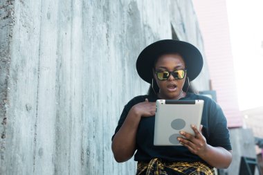 Güzel kıvırcık Afrikalı Amerikalı bir kızın portresi. Arka planda duruyor ve elinde dijital tablet var. Tablet bilgisayar konsepti olan çekici genç bir kadın.