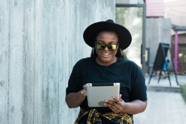 Güzel kıvırcık Afrikalı Amerikalı bir kızın portresi. Arka planda duruyor ve elinde dijital tablet var. Tablet bilgisayar konsepti olan çekici genç bir kadın.