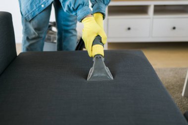 Temizlik şirketi çalışanı, profesyonel malzemelerle mobilyaların tozunu alıyor. Erkek kol temizleme koltuğu ve elektrikli süpürge.