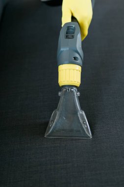 Temizlik şirketi çalışanı, profesyonel malzemelerle mobilyaların tozunu alıyor. Erkek kol temizleme koltuğu ve elektrikli süpürge.